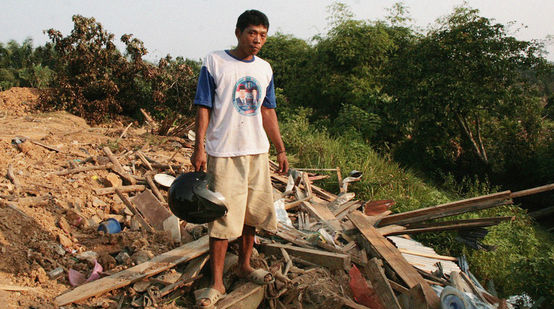 Un paysan se tient devant son village en ruines