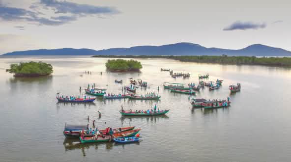 Des bateaux se rassemblent dans l’embouchure du fleuve. On aperçoit en arrière-plan des petites iles ainsi que les rives du fleuve.