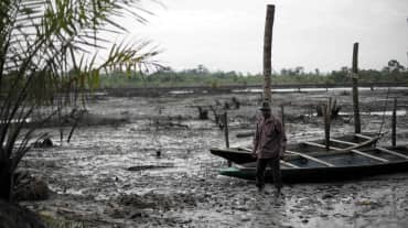 Un homme se tient debout dans le lit d’une rivière polluée par le pétrole dans le delta du Niger