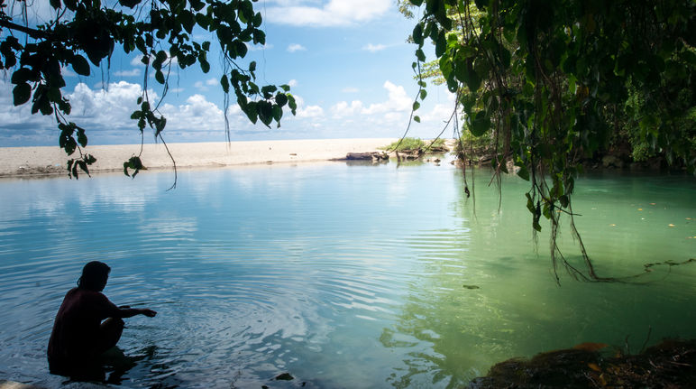 Une femme est assise dans l’eau dans une baie bordée de sable et de rochers