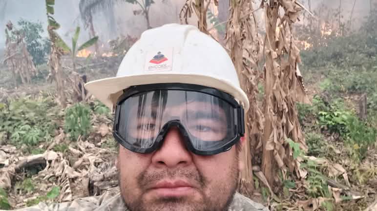 Julio Yeguaori, l’un des meilleurs trompettistes de Bolivie, professeur et chef de l’orchestre symphonique d’Urubicha, aide à éteindre les incendies Un homme portant un casque et des lunettes de protection regarde la caméra, tandis que des buissons brûlent et que de la fumée s’élève à l’arrière-plan