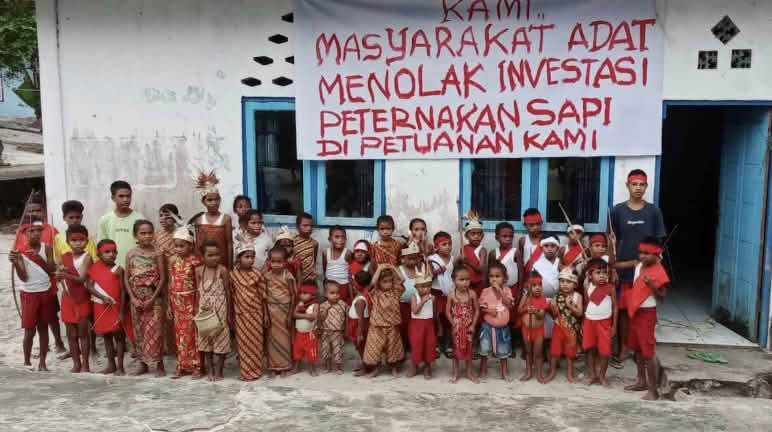 « Nous, autochtones, refusons que des investissements dans l’élevage bovin soient réalisés sur nos terres ancestrales ! » Groupe d’enfants devant une école sur laquelle est accrochée une banderole avec un message en indonésien
