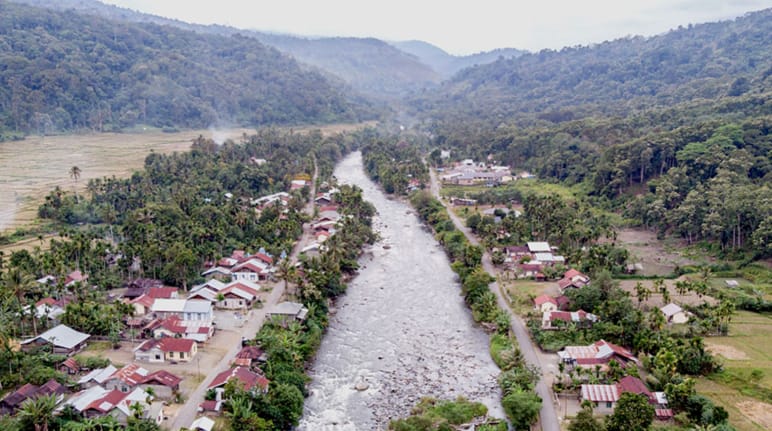 Vue aérienne d’une rivière traversant un village, avec des montagnes en arrière-plan