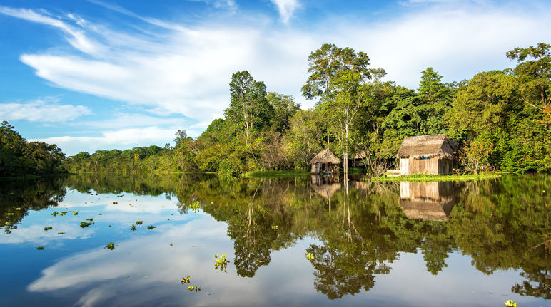 La forêt amazonienne et une cabane en bois se reflètent dans l’eau du fleuve Yanayacu au Pérou