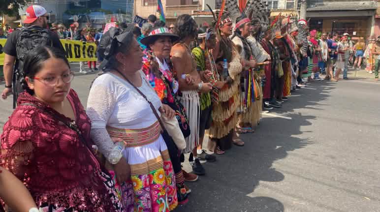 Des femmes et des hommes indigènes vêtus de couleurs vives forment une chaîne lors d’une manifestation