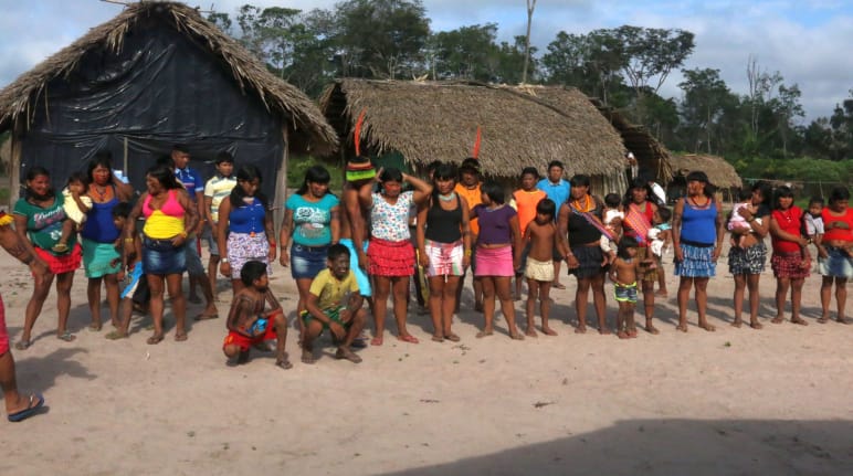 Des indigènes Kaapor se tiennent devant deux huttes dans la forêt tropicale