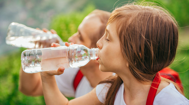 Une jeune fille en train de boire de l’eau dans une bouteille en plastique jetable PET