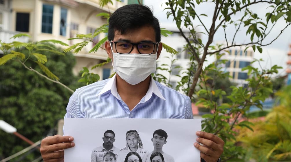 Un jeune homme brandit une affiche avec les photos des 6 militants de Mother Nature emprisonnés