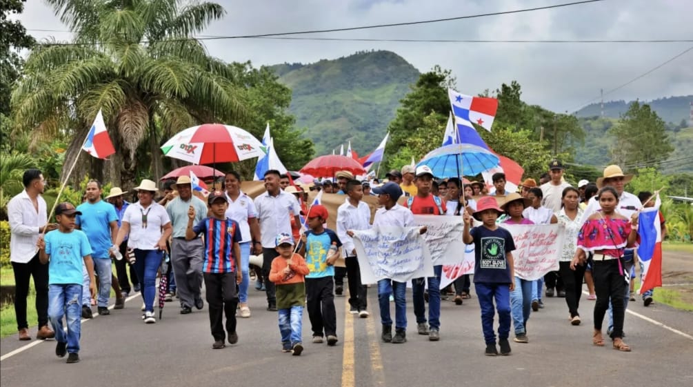 Des personnes défilent sur une route de campagne au Panama avec des bannières, des drapeaux du Panama et des parapluies assortis