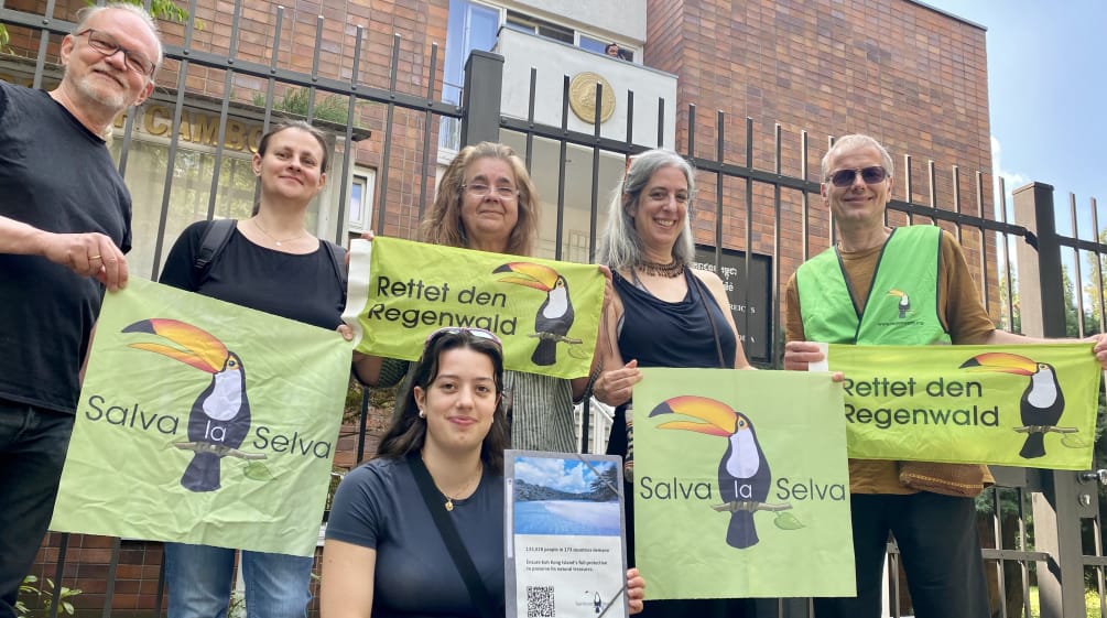 6 personnes posent devant la grille du bâtiment de l’ambassade du Cambodge à Berlin, tenant des bannières de l’association "Rettet den Regenwald"