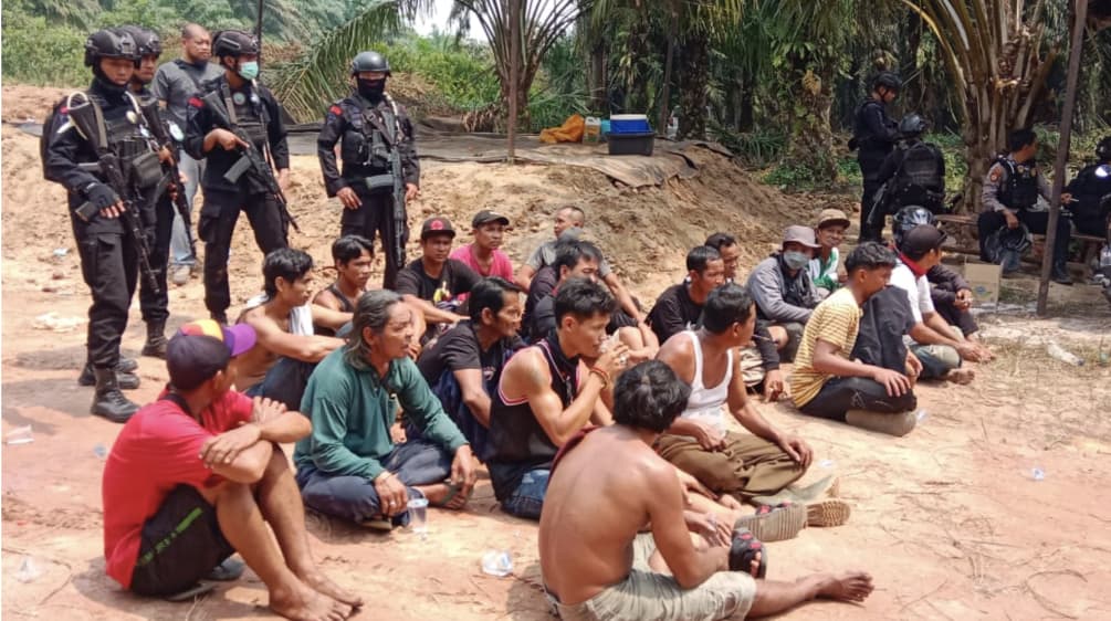 Des autochtones du peuple Dayak sont assis par terre, avec des policiers lourdements armés derrière eux