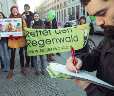 Au premier plan un homme signe une pétition de Sauvons la forêt. En arrière plan des activistes avec leurs banderoles et pancartes devant une boutique Nespresso à Berlin.