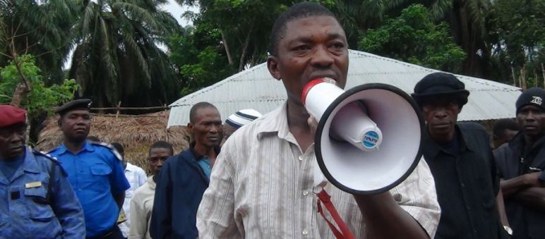 Résister à l’accaparement des terres et à l'industrie de l'huile de palme est de plus en plus risqué en Sierra Leone Surveillé par des militaires, l’ancien parlementaire de la Sierra Léone Hon. Musa Sama, parle dans un mégaphone dans une plantation de palmiers à huile