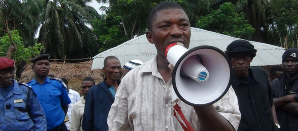 Non à l’intimidation des habitants faisant valoir leurs droits contre l’accaparement de leurs terres ! Surveillé par des militaires, l’ancien parlementaire de la Sierra Léone Hon. Musa Sama, parle dans un mégaphone dans une plantation de palmiers à huile