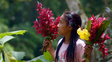 Une jeune fille Kichwa se tenant de profil porte un bouquet de fleur dans chaque main