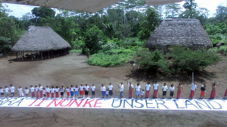 Vue aérienne. Des amérindiens d'Amazonie équatoriale ont déployé devant eux sur le sol une immense banderole sur laquelle est inscrit le message « C'est notre terre »