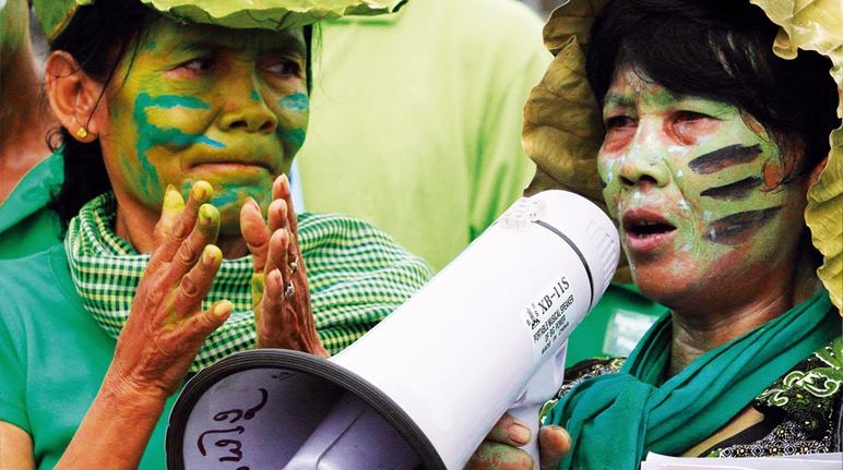 Gros plan sur deux femmes maquillées de bleu et de vert lors d'une manifestation. L'une tape dans les mains, l'autre parle dans un mégaphone