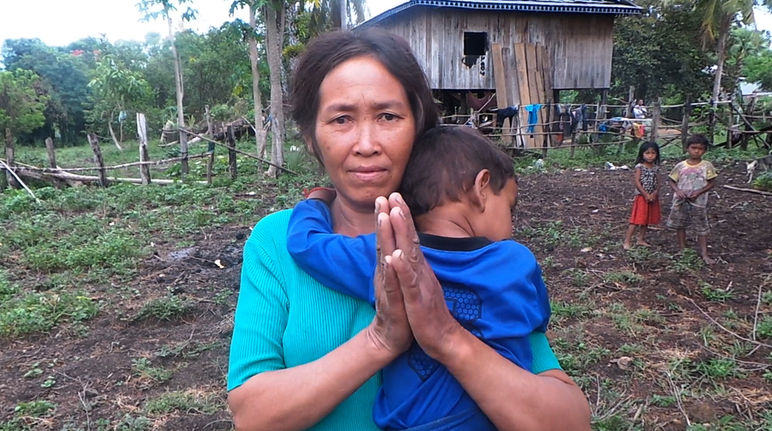 Une femme chassée de ses terres se tient devant un habitat de fortune (qu’on lui souhaite) provisoire. Avec son enfant accroché à son cou, elle tient ses mains jointes pour demander de l’aide.