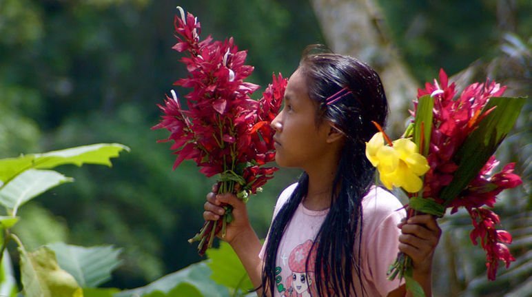 Une jeune fille Kichwa se tenant de profil porte un bouquet de fleur dans chaque main