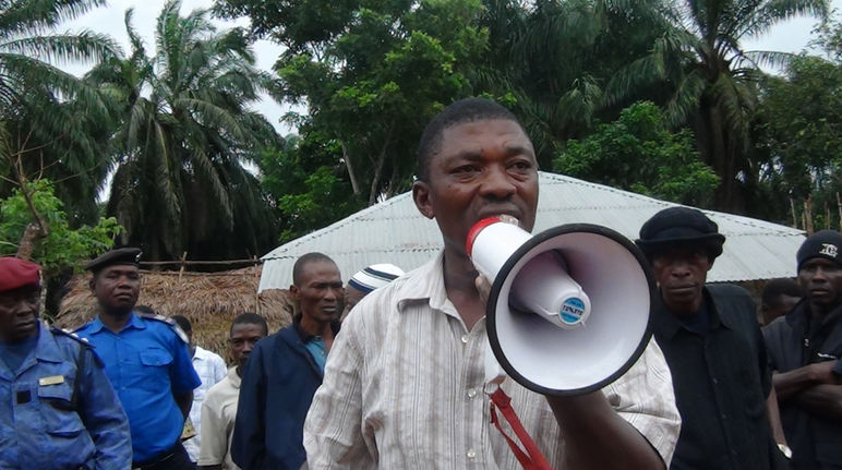 Non à l’intimidation des habitants faisant valoir leurs droits contre l’accaparement de leurs terres ! Surveillé par des militaires, l’ancien parlementaire de la Sierra Léone Hon. Musa Sama, parle dans un mégaphone dans une plantation de palmiers à huile