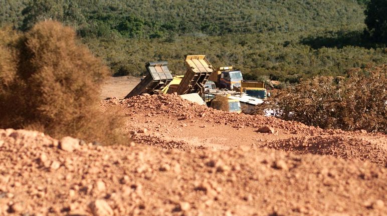 L'extraction de bauxite menace d'assèchement l'ensemble de la zone forestière et ses 250.000 habitants Terre rouge au premier plan séparée des forêts en contrebas par des camions chargeant de la bauxite